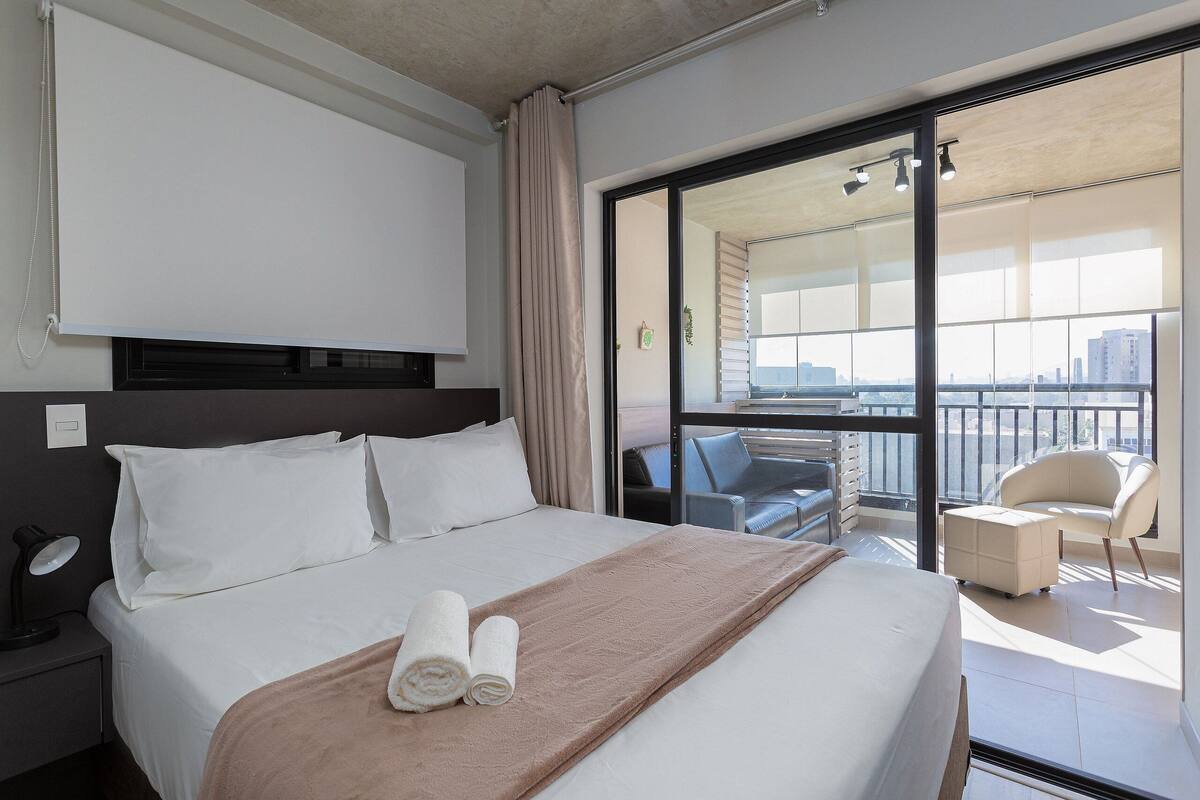 Ein Hotelzimmer mit einem Bett, einem Schreibtisch mit Lampe, einem Sessel, einem Balkon mit Aussicht und einer Glastür.