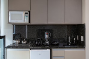 A kitchen with a microwave, toaster, blender, and a refrigerator.