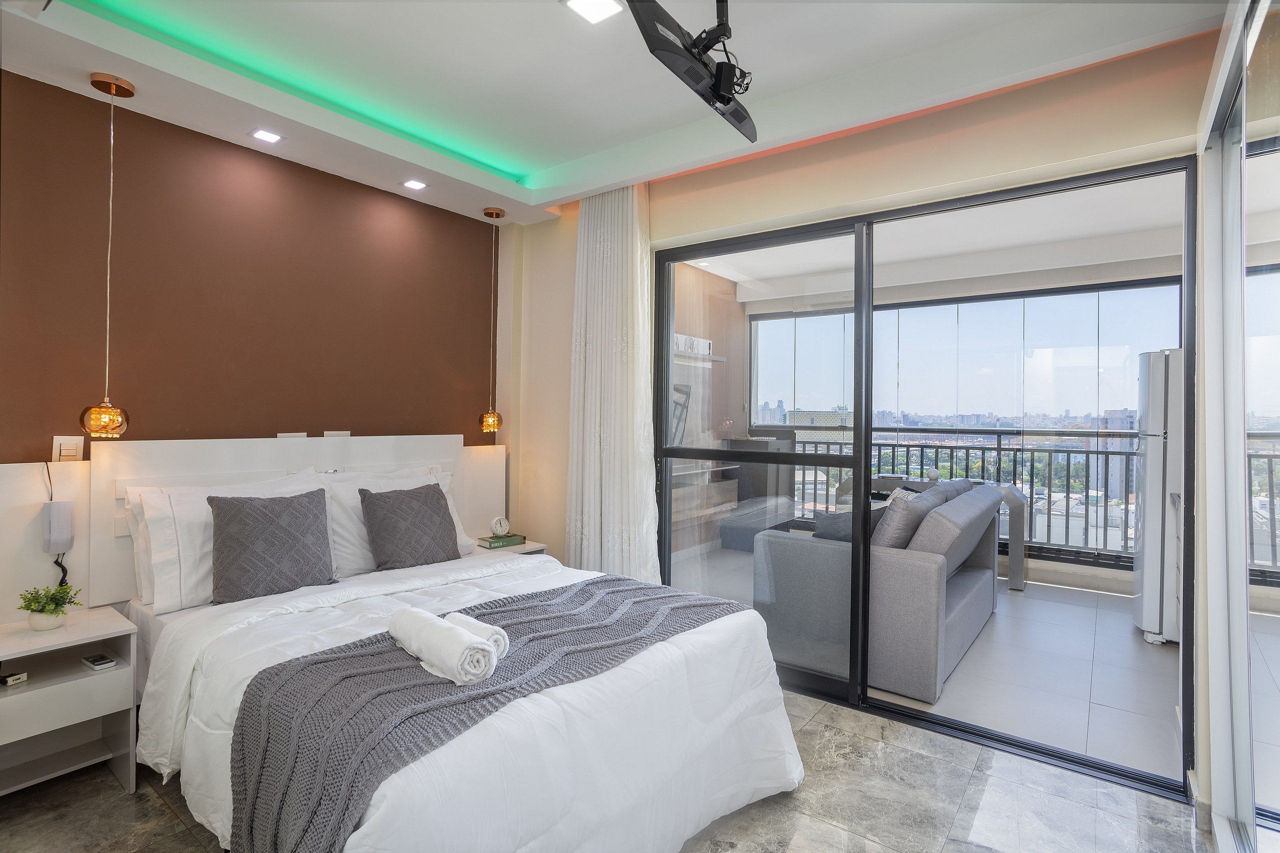 A modern hotel room with a large bed, a balcony with a sofa, and a city view.