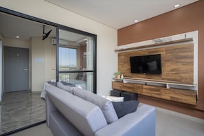Un salon moderne avec un canapé gris, un téléviseur à écran plat fixé sur un mur en bois et une porte-fenêtre coulissante donnant sur un balcon.