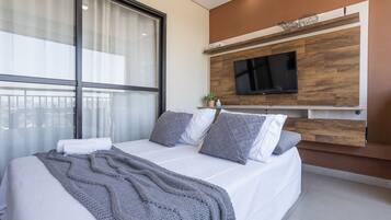 Um quarto moderno com uma cama grande, televisão fixada em uma parede de madeira e uma janela com cortinas.