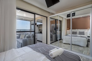 A hotel room with a balcony, a bed, a sofa, and a sliding glass door leading to a balcony.