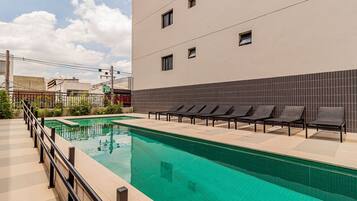 Piscina com espreguiçadeiras, um deck revestido de azulejos e um edifício com fachada em azulejo.