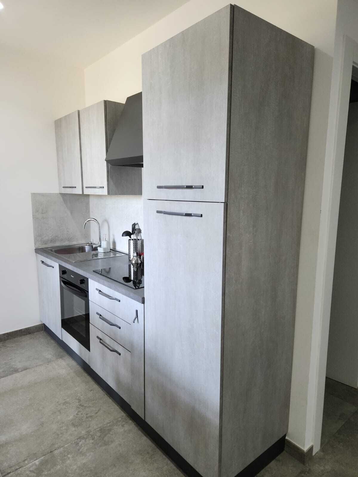 A modern kitchen with grey cabinets, a stainless steel sink, and a built-in oven.