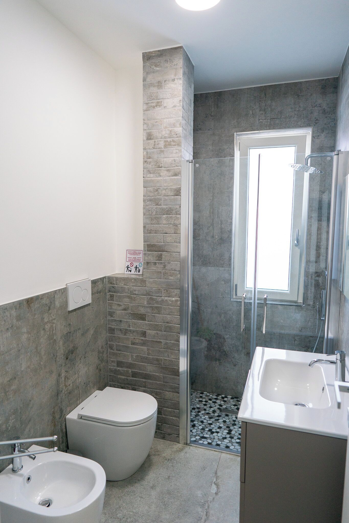 Bagno con WC, bidet e lavandino, dotato di cabina doccia in vetro e finestra.