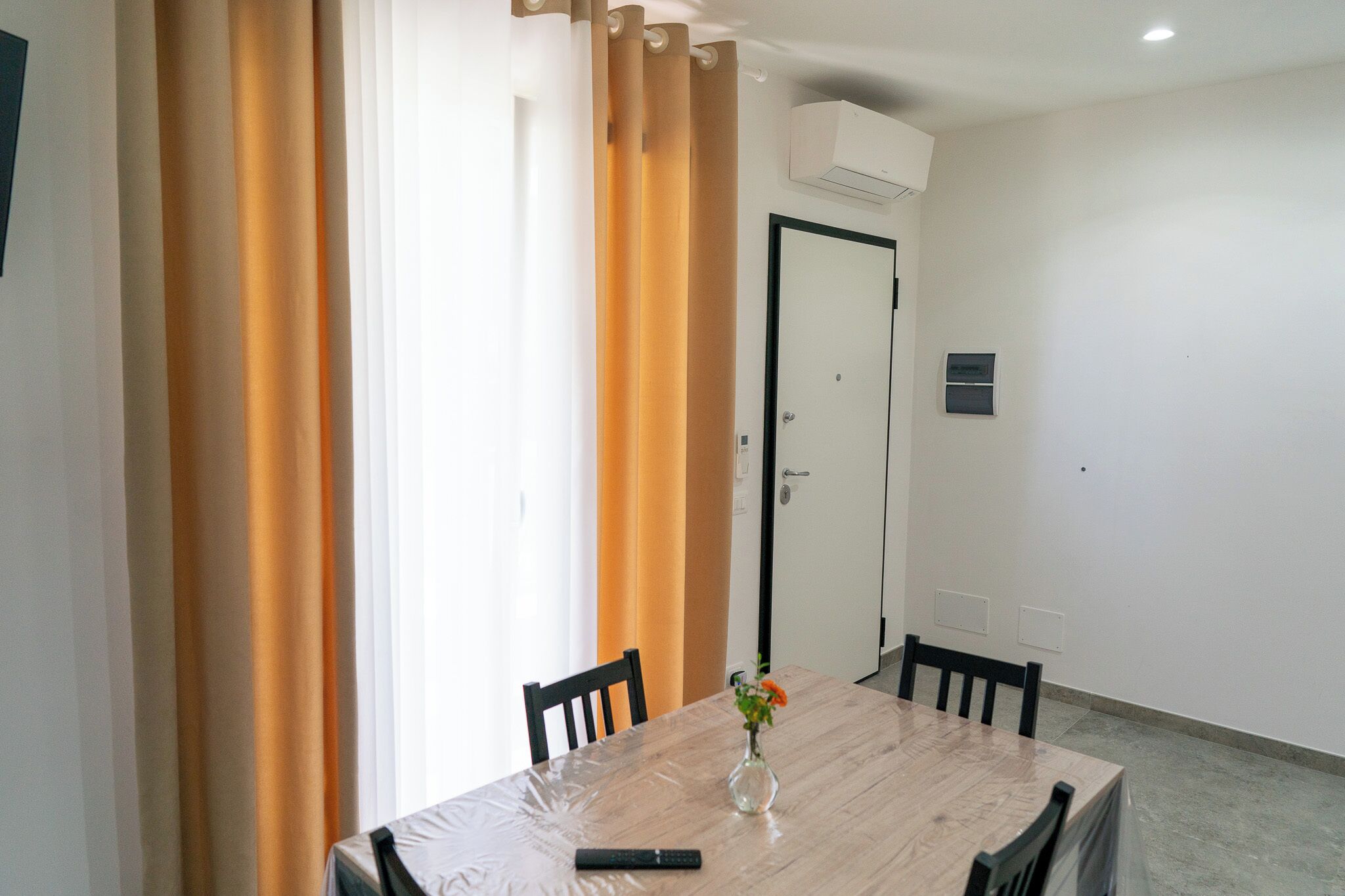 Habitación de hotel con mesa de comedor, sillas, un florero con flores, un control remoto y una puerta cerrada.