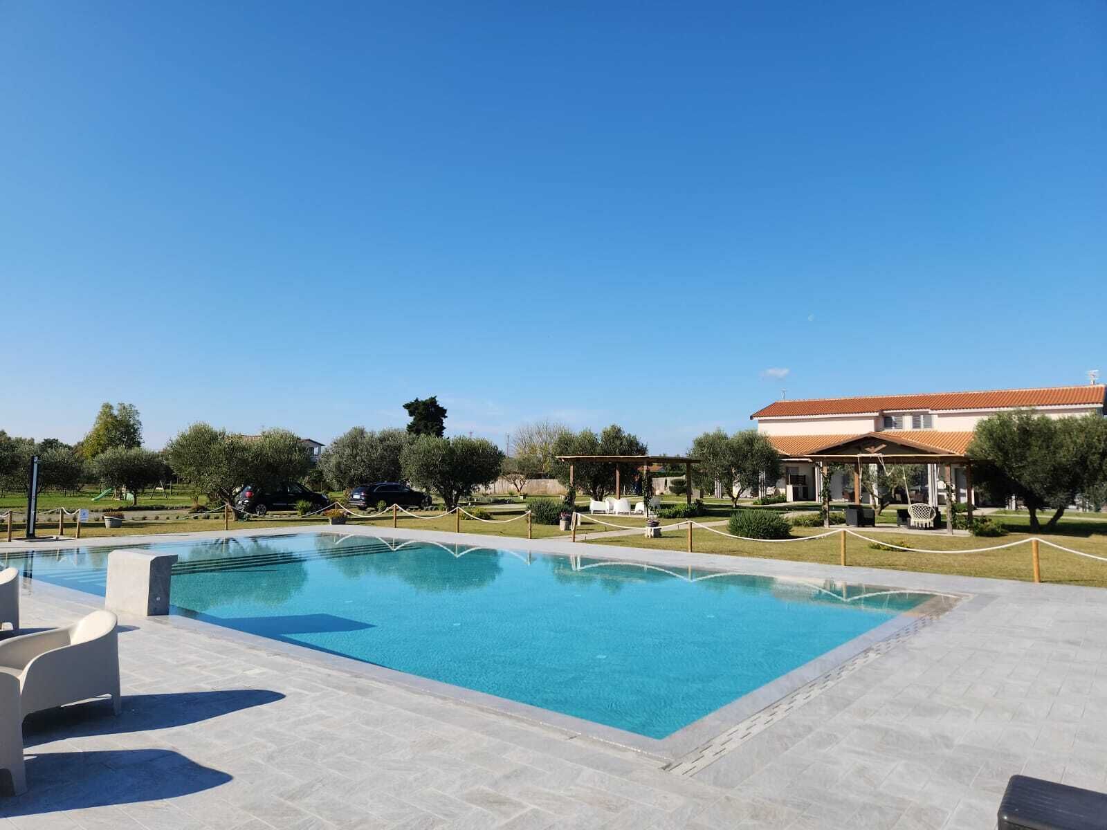Une piscine rectangulaire, bordée d’une terrasse carrelée, entourée d’une clôture basse et dotée d’un espace de repos abrité.