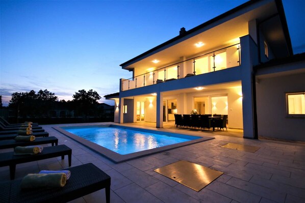 Une maison à deux étages avec une piscine, un espace extérieur aménagé pour se détendre et une terrasse bien éclairée.