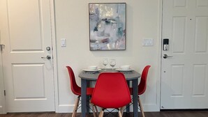 A dining area with a round table, four red chairs, and a modern abstract painting on the wall.