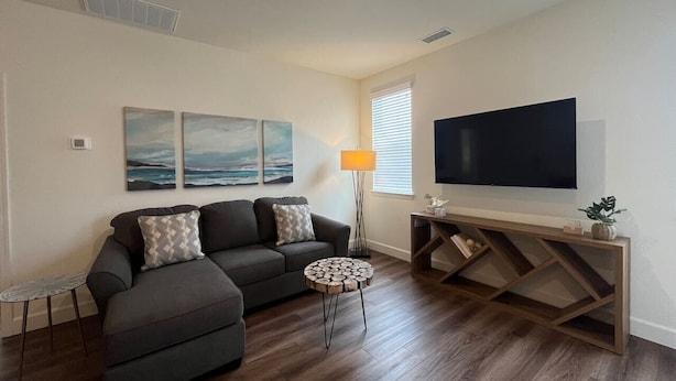 A modern living room with a sectional sofa, a round coffee table, a TV on a wooden stand, and artwork on the wall. - Lakeview Retreat: Golf, Fish, & Explore the Trails (Sparks)