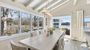 Un comedor espacioso con una mesa larga, numerosas sillas y un candelabro. Amplias ventanas ofrecen vistas al exterior.