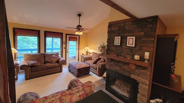 A cozy living room with a stone fireplace, two sofas, a patterned ottoman, and a ceiling fan. - Cozy Loft nestled atop of Snowshoe (Snowshoe)