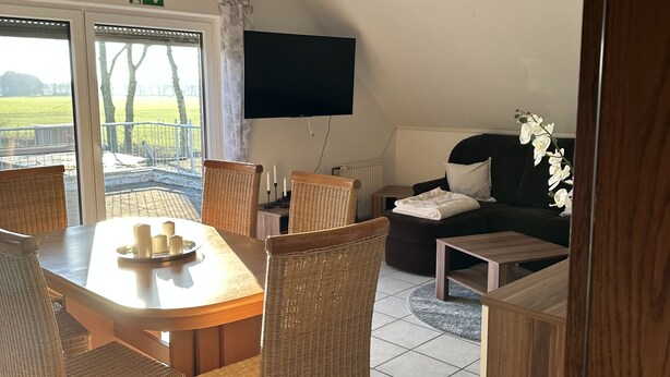 A room with a dining table, wicker chairs, a sofa, a TV, and a view of the outdoors. - Vacation apartment Haren /Ems for up to 6 people  (Haren (Ems))