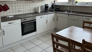 A modern kitchen with white cabinets, a built-in oven, a coffee maker, and a window with curtains. - Vacation apartment Haren /Ems for up to 6 people  (Haren (Ems))