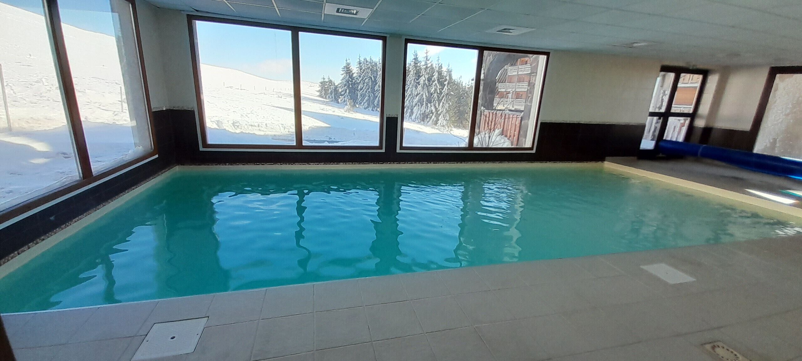 Une piscine intérieure offrant une vue dégagée sur un paysage enneigé grâce à de grandes fenêtres.