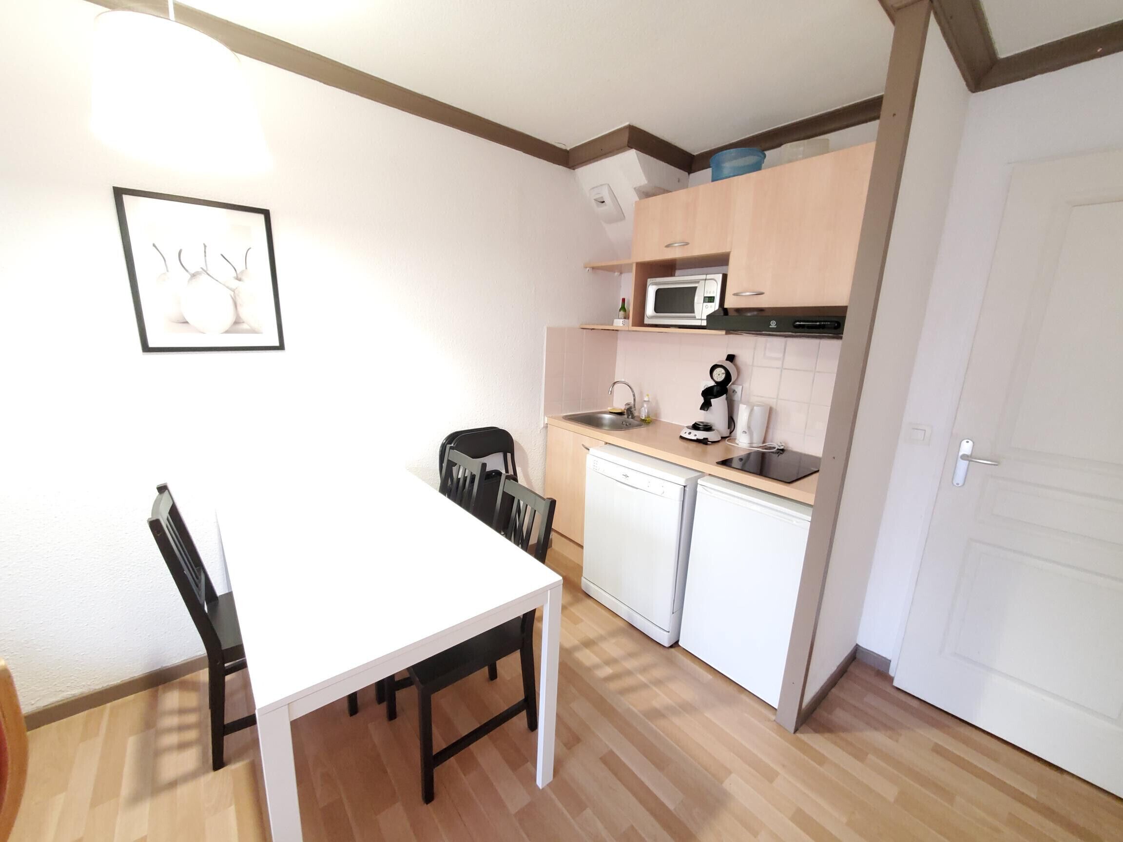 A compact kitchen with a white table and chairs, a microwave, a coffee maker, and a dishwasher.