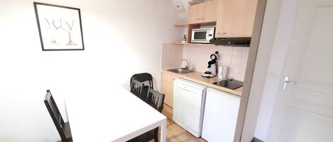 A compact kitchen with a white table and chairs, a microwave, a coffee maker, and a dishwasher.