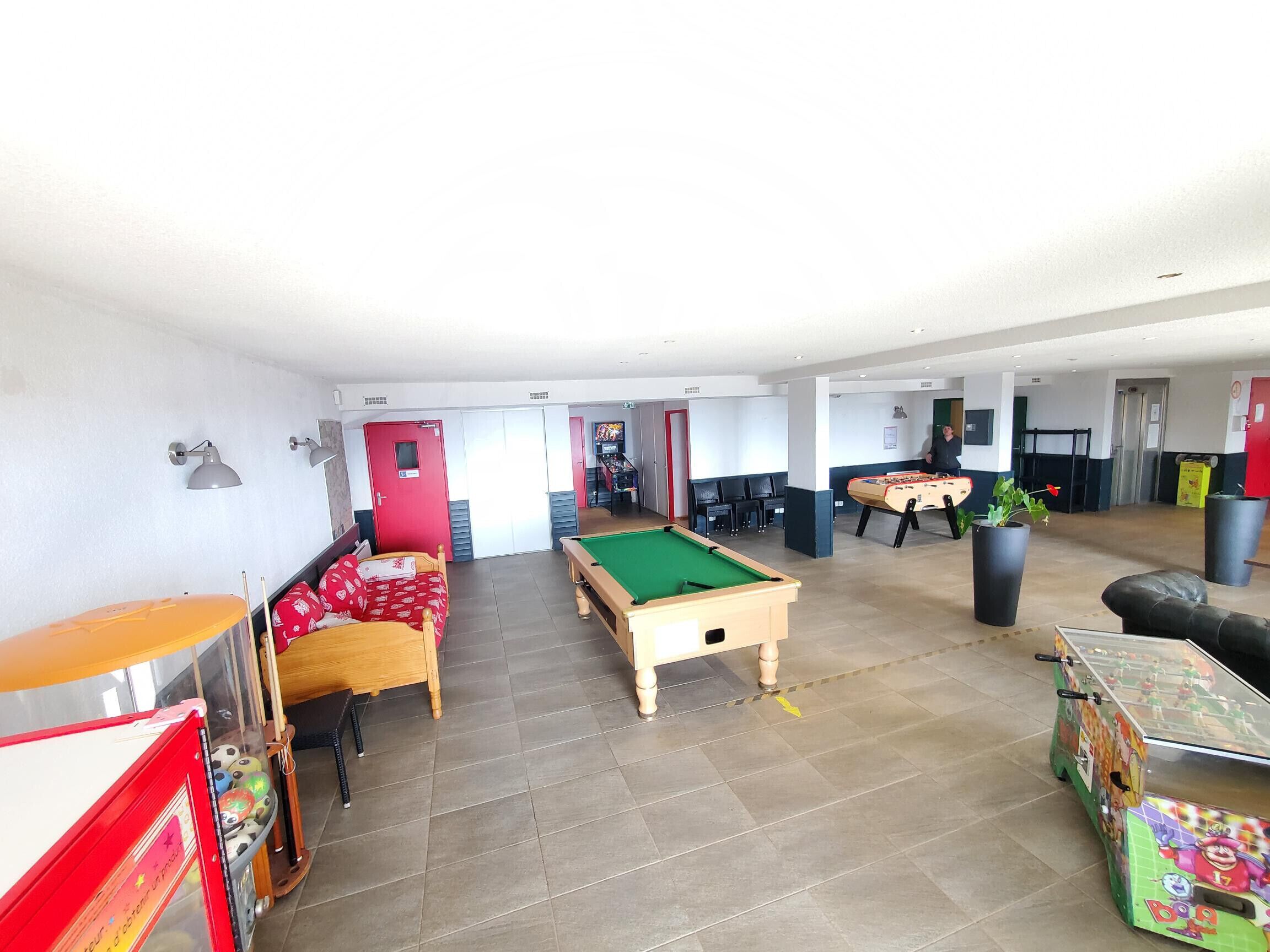 A room with a pool table, a foosball table, and a billiards table. There are chairs and a sofa.
