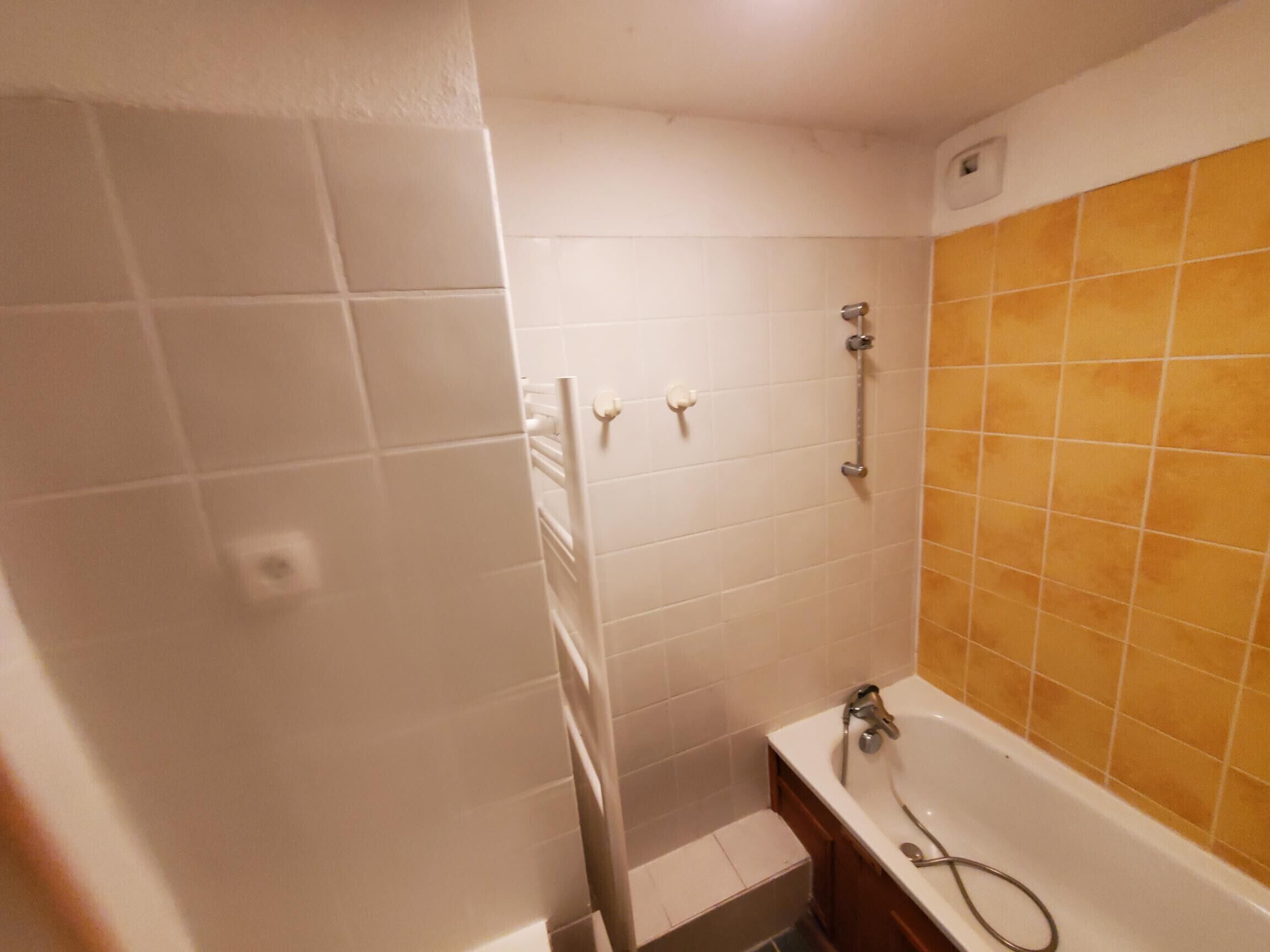 A bathroom with white tiles, a yellow-tiled shower area, a white bathtub, and a wooden vanity.