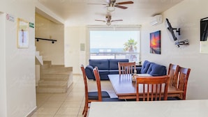 A dining area with a table and chairs, a ceiling fan, and a view of the ocean through large windows.