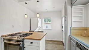 A kitchen with a central island, white cabinetry, a stove, and a dishwasher. - 1920's Spanish Revival Home (Tustin)
