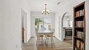 A dining area with a wooden table and chairs, a chandelier, and a bookshelf with books. - 1920's Spanish Revival Home (Tustin)
