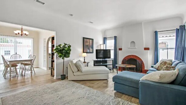 A living room with a sofa, a TV, a fireplace, and a dining area with chairs and a table. - 1920's Spanish Revival Home (Tustin)