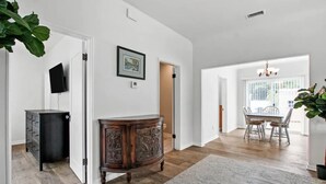 A spacious room with hardwood flooring, a large wooden cabinet, a dining area with a table and chairs, and a chandelier. - 1920's Spanish Revival Home (Tustin)
