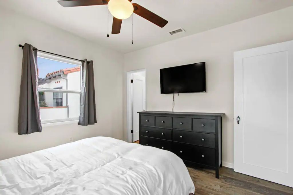 Ein Schlafzimmer mit einem Bett, einem Deckenventilator, einem an der Wand montierten Fernseher und einer Kommode.