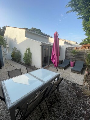 Un patio con mesa y sillas de vidrio, un paraguas rosa y una zona de estar con cojines.