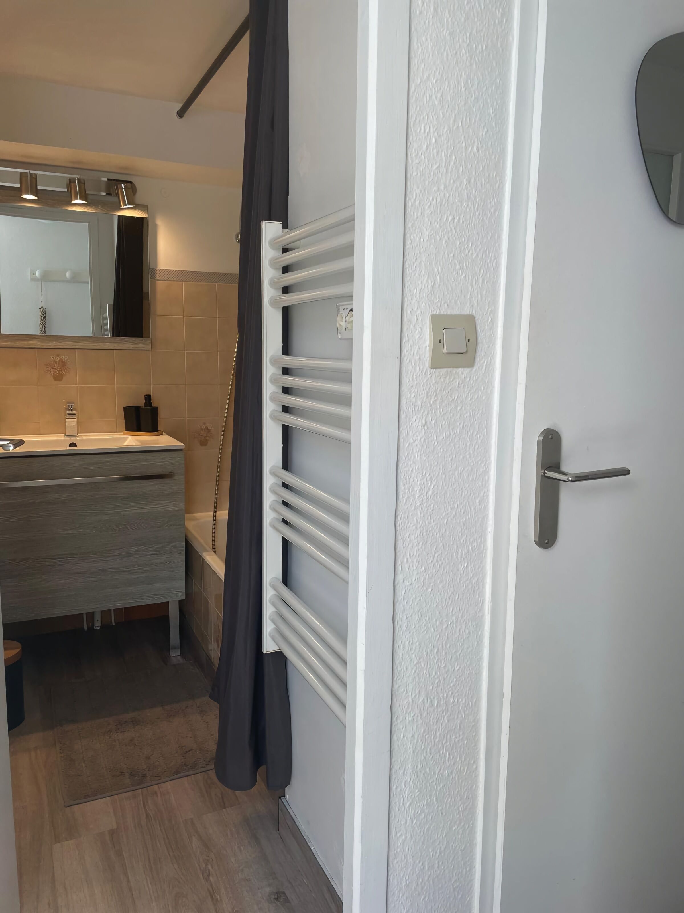 A bathroom with a sink, mirror, towel rack, and a door with a handle.
