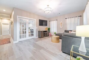 Relax in this stylish living room with a sofa, coffee table, and flat-screen TV, leading to an outdoor area through a large sliding glass door.