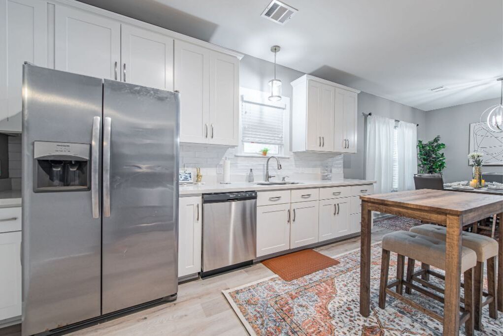 A modern kitchen with stainless steel appliances, white cabinetry, and a dining area with a wooden table and bench.