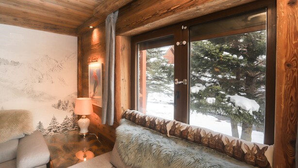 A cozy room with a wooden ceiling, a large window with a view of snow-covered trees, a plush sofa with a fur throw, and a lamp on a wooden table. - Apartment chalet vallée d'incles Andorra (Canillo)