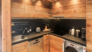 A modern kitchen with wooden cabinetry, a black countertop, and stainless steel appliances including a dishwasher and a coffee maker. - Apartment chalet vallée d'incles Andorra (Canillo)