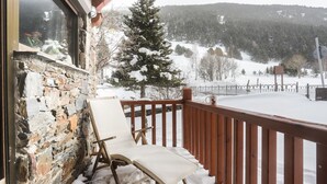 A stone exterior wall, a wooden deck with a white chair, and a snow-covered landscape with a tree. - Apartment chalet vallée d'incles Andorra (Canillo)