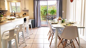 A modern kitchen with white cabinets, a dining area with a table set for four, and a view of a garden through a glass door.