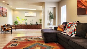 A modern living room with a sectional sofa, a patterned rug, a brick accent wall, and a potted plant.