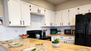 A modern kitchen with white cabinets, a black refrigerator, a microwave, and a stove. There are plates, glasses, and a plant on the counter.