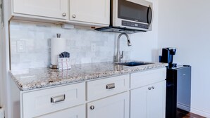 A kitchen with white cabinets, a granite countertop, a built-in microwave, a sink, and a coffee machine. - Unit 27 Waena Inn - Maui Private Suite (Wailuku)