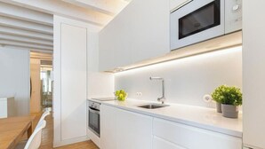 A modern kitchen with white cabinetry, a stainless steel sink, a microwave, and a small potted plant.