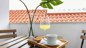 A wooden table with a tray holding a glass of yellow drink, a white mug, and a pastry. A tall green plant is beside the table.