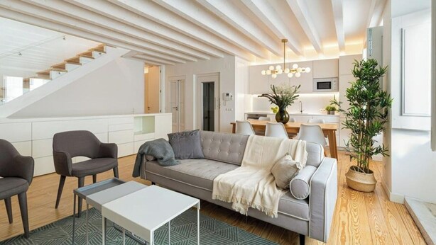 A modern living room with a grey sofa, a coffee table, and a staircase leading to an upper floor.