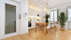 A modern kitchen with white cabinets, a wooden dining table, and a hanging light fixture.
