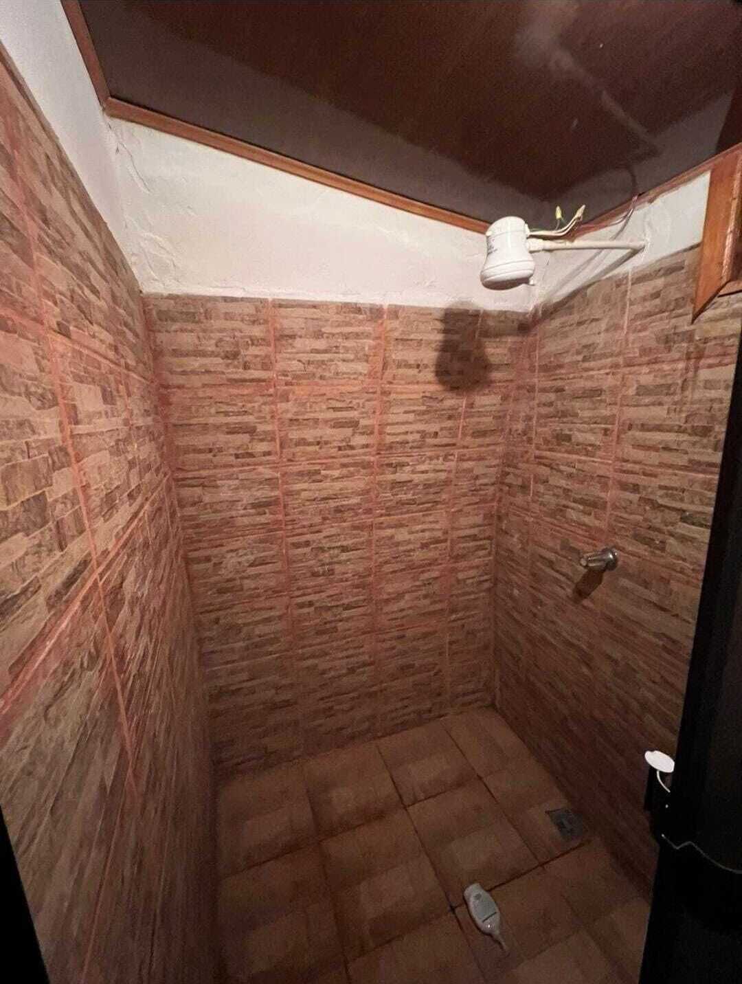 A small, enclosed bathroom with brick-patterned walls and a tiled floor.