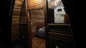 A cozy, wooden cabin interior with a bed, a small table, and a door leading to another room. - Cabañas La Laguna Lodge (Corralillo)