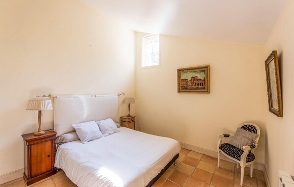 A bedroom with a bed, two bedside tables, a chair, a window, and a framed picture on the wall.