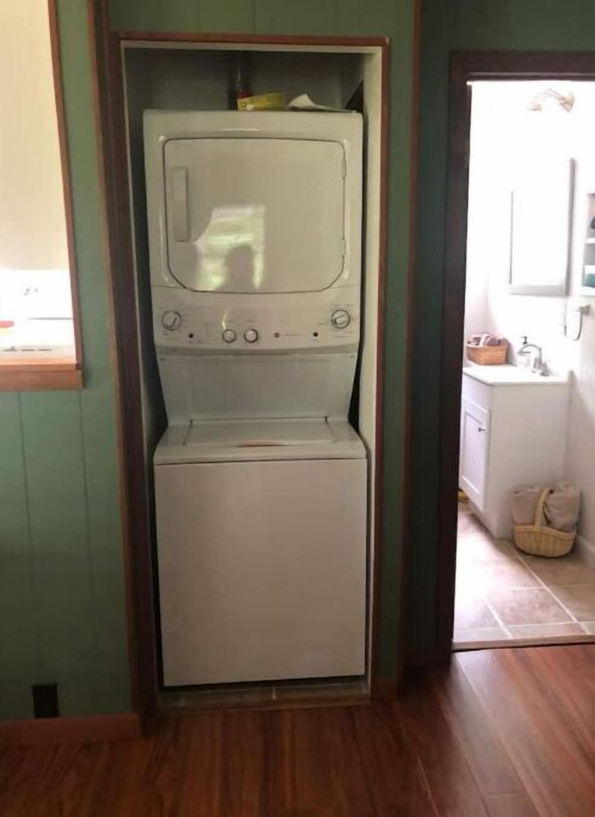 Un lavadero pequeño y blanco con lavadora y secadora integradas, suelo de madera y pared verde.