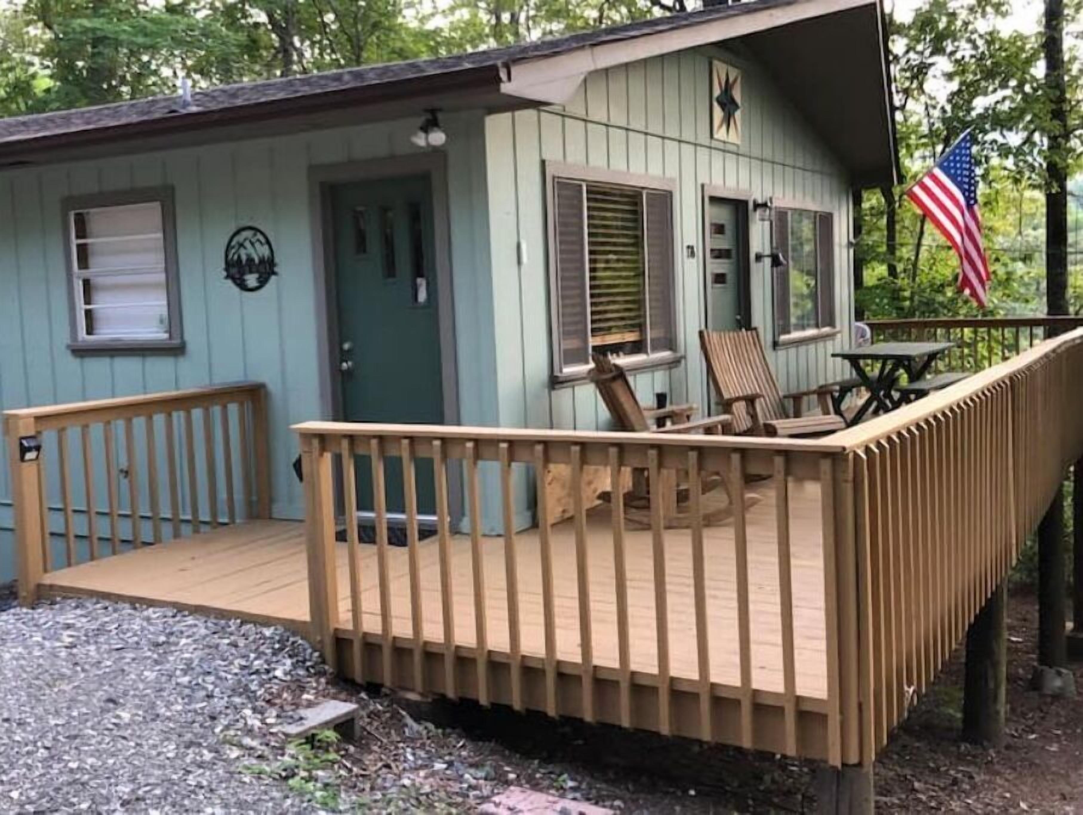 Una piccola baita blu chiaro con un portico in legno e due sedie.