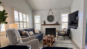 A living room with a fireplace, a television, and a dining area with a table and chairs. - Seahorse Cottage Luxe (Oxnard)